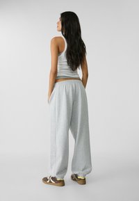 Pantalons de survêtement gris clair avec des poignets élastiques, dotés de poches latérales et d'une coupe confortable, associés à un débardeur blanc ajusté.