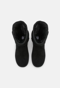 Para czarnych zimowych butów z puszystym wyściółką wewnętrzną, widziana z góry na neutralnym tle.