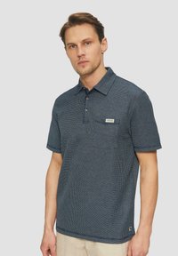 Dunkelblaues Polohemd mit kurzen Ärmeln, strukturiertem Muster, Knopfleiste mit drei Knöpfen, Brusttasche und einem kleinen Markenlabel auf der Tasche.