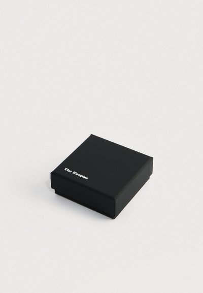 Čierna šperkovnica s logom "The Kooples" v bielej farbe v ľavom hornom rohu, umiestnená na jednoduchom svetlom pozadí.