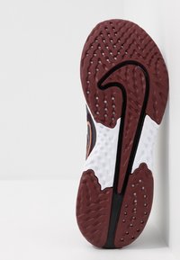 Musta urheilukenkien pohja, jossa on teksturoitu punainen kumipohja, valkoinen välipohja ja erottuva kaartuva musta raidoitus reunan varrella.