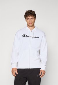Hvit zip-up hettegenser laget av bomullsblanding, med en stor svart "Champion" logo på brystet, med snorhette og frontlommer.
