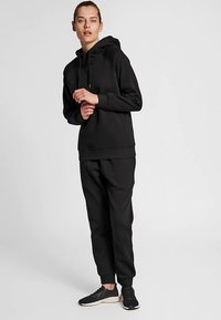 Svart hoodie med dragsko, lös passform; matchas med matchande joggingbyxor. Materialet verkar mjukt och slätt med ribbade muddar och midjeband.