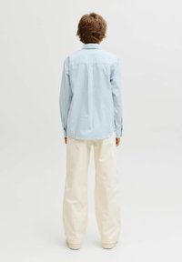 Světle modrá pruhovaná košile s klasickým límcem, dlouhými rukávy a rovnými okraji. Kombinována s krémově bílými kalhotami širokého střihu.