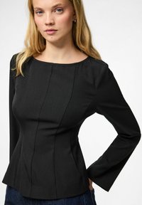 Maglia nera a maniche lunghe con silhouette aderente, presenta dettagli a pieghe, scollatura rotonda e texture del tessuto liscia.