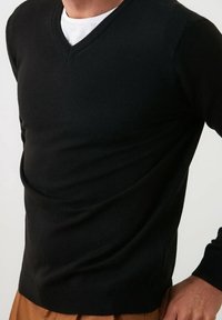 Pull noir à col en V fabriqué à partir d'un tissu tricoté doux, présentant une silhouette ajustée et des poignets côtelés, avec une texture lisse et des coutures nettes.