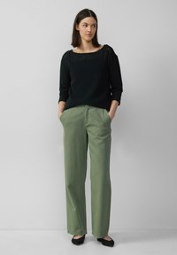 Zwarte gebreide trui met een open steekpatroon en een wijde halslijn, gecombineerd met lichtgroene palazzo broek. Zwarte ballerina's maken de outfit compleet.