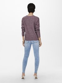 Lila gerippter Strickpullover, lässiger Schnitt, runder Ausschnitt, kombiniert mit hellblauen Skinny Jeans mit ausgefranstem Saum und weißen High Heels.
