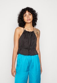 Top preto com alças, com decote franzido e bainha peplum, feito de tecido suave. Combinado com calças largas de cetim azul brilhante.