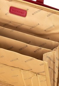 Wnętrze brązowej torby z wieloma kieszeniami, siatkową sekcją oraz markowym oznaczeniem w kolorze czerwonym. Gładki materiał z powtarzającym się wzorem logo.