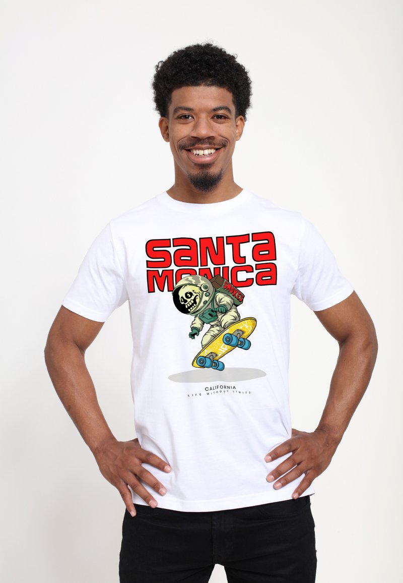 Bílý bavlněný tričko s barevným grafickým vzorem kostlivce ve skafandru, jak jezdí na žlutém skateboardu, s nápisem "SANTA MONICA".