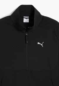 Giacca nera con zip e colletto alto, caratterizzata da un pannello testurizzato e un logo riflettente sul petto. Tessuto liscio con design a contrasto.