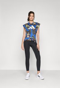 Haut bleu vif avec motif de papillons, manches courtes volumineuses, associé à des leggings noirs et des chaussures de sport blanches.