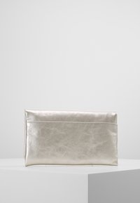 Pochette rectangulaire métallique argentée avec une texture lisse, exposée sur un piédestal blanc contre un fond uni.