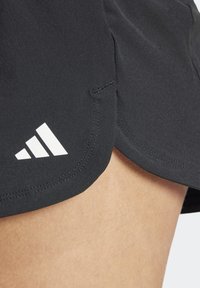 Svarta träningsshorts med en böjd fåll, med en vit triangulär logotyp. Materialet verkar slätt, med synliga sömmar.