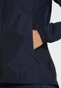 Marins blå vattentät jacka med långa ärmar, elastiska muddar, sidofickor och en tygetikett i fållen. Slät yta och lättviktig design.