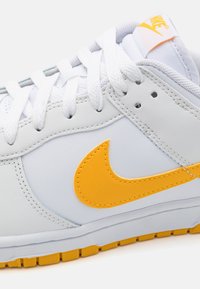 Weiße Leder-Sneaker mit orangefarbenen Akzenten, ausgestattet mit einem auffälligen Swoosh-Logo, flachen Schnürsenkeln und einer strukturierten Gummisohle für guten Halt.