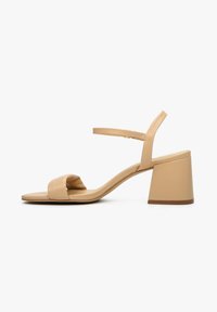 Beżowe skórzane sandały na obcasie z szerokim paskiem z przodu, cienkim paskiem na kostkę oraz kwadratowym obcasem, charakteryzujące się gładką teksturą i minimalistycznym designem.