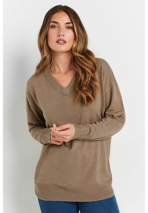Beige knitted sweater with a v-neck, long sleeves, and ribbed cuffs. Soft texture and relaxed fit, paired with blue denim jeans.