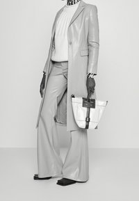 Vaaleanharmaa nahkatakki, ribattu valkoinen villapaita, harmaat nahkahousut ja mustat hanskat. Pitelee pientä valkoista laukkua, jossa on mustia yksityiskohtia.