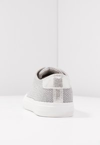 Hopeasävyiset verkkokengät, joissa on teksturoitu muotoilu, metallinen kantaosa ja valkoinen kumipohja. Minimalistinen ja moderni ulkonäkö.