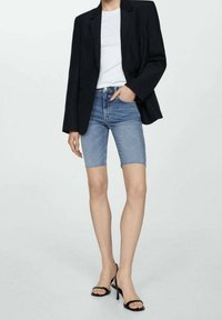 Musta bleiseri valkoisen T-paidan päällä, yhdistettynä vaaleansinisiin farkkushortseihin, joissa on kuluneet reunan. Mustat korkokengät viimeistelevät asun.