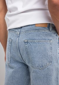 Jeans in denim azzurro con gamba affusolata, dotati di tasche posteriori con un motivo ad arco cucito e un'etichetta in pelle sulla cintura.