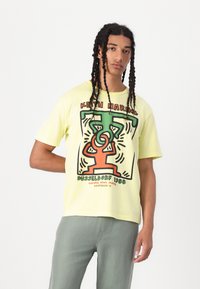 Yellow cotton t-shirt featuring a graphic print by Keith Haring in red, green, and black. Relaxed fit with short sleeves.