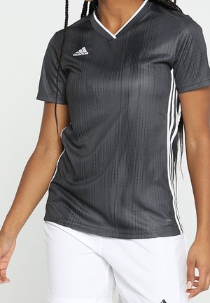 Czarna sportowa koszulka Adidas z białymi paskami po bokach, noszona z białymi szortami Adidas na osobie z zaplecionymi włosami.