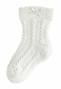 Calzino bianco lavorato a maglia con un motivo testurizzato, bordo a costine e orlo arricciato, decorato con un fiocco in argento.