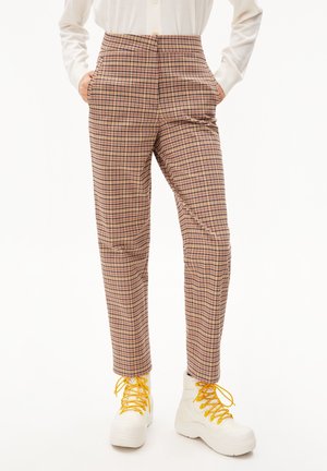 Pantalon à carreaux texturé de couleur claire, taille haute, avec des poches latérales et une coupe slim, accompagné de baskets blanches avec des lacets jaunes.