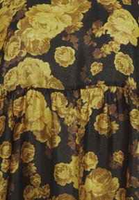 Tissu noir avec des roses jaune doré brillantes et de petites feuilles marron, avec une couture froncée créant un effet volanté.
