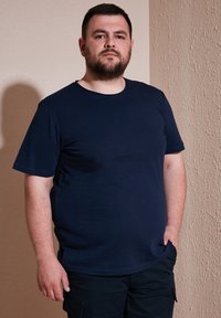 Tricou scurt din bumbac de culoare albastru închis, cu mâneci scurte, având un guler rotund și un croi lejer. Potrivit pentru îmbrăcăminte casual.