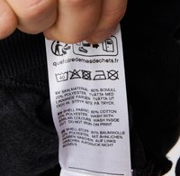 Étiquette en tissu noir avec des instructions d'entretien et la composition du matériau : 80 % coton, 20 % polyester. Comprend des icônes de lavage et du texte en plusieurs langues.