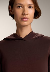 Brązowa bluzka z kapturem o prążkowanej fakturze, z delikatnym dekoltem i czystymi liniami, koncentrująca się na prostocie i nowoczesnym designie.