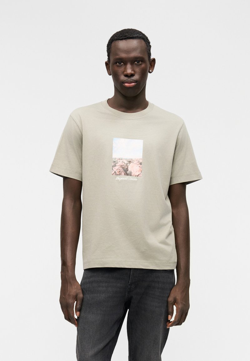 Ανεπίσημο κοντομάνικο t-shirt σε ανοιχτό ελιά, με ορθογώνιο γραφικό φύσης και λεπτομέρεια κειμένου στο κάτω μέρος. Κατασκευασμένο από απαλό βαμβακερό υλικό.