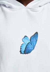 Sudadera blanca con un gran gráfico de una mariposa azul detallada. La mariposa tiene alas prominentes con diferentes tonos de azul y acentos en negro.