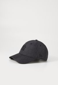 Black cap with hexagonal quilted texture, featuring embroidered logo on the front and a curved brim. Constructed from a durable fabric.