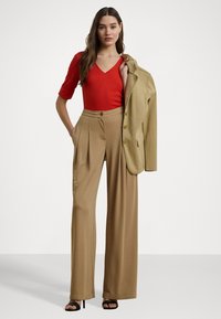 Červený přiléhavý top, béžové široké kalhoty s vysokým pasem a záhyby, a béžový sako. Černé sandály na vysokém podpatku dotvářejí outfit.