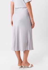Lichtgrijze, middellange satijnen rok met een vloeiende silhouet, subtiele scalloped zoom en een gladde textuur. Draagt met witte open teen hakken.