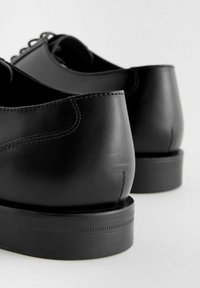 Black leather shoes with a smooth texture, rounded backs, and a flat rubber sole, featuring subtle stitching details and a sleek design.