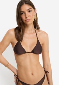 Κορυφή μπικίνι καφέ σε σχήμα τριγώνου με χρυσή λεπτομέρεια σε σχήμα ήλιου, ρυθμιζόμενους δεσμούς και λεία υφή. Διαθέτει ελάχιστη κάλυψη και κομψό σχεδιασμό.