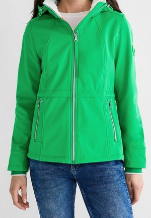 Femme portant une veste zippée vert vif avec des poches avant et un jean bleu, vue des épaules aux hanches.