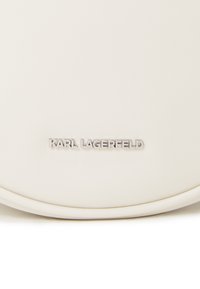 Sac en cuir blanc rond avec le logo "KARL LAGERFELD" embossé en argent. Texture lisse, design minimaliste, sans motifs ou accents supplémentaires.