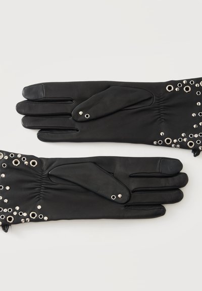 Gants en cuir noir avec œillets et clous argentés sur les poignets, présentés côte à côte avec les doigts étendus.