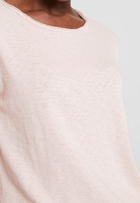 Top corto rosa chiaro a maniche corte realizzato in tessuto morbido, con scollatura ampia e superficie leggermente strutturata. Vestibilità casual e rilassata.