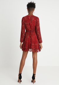 Robe rouge à manches longues, imprimé léopard et jupe fluide. Taille élastique et ourlet à volants. Associée à des talons noirs.