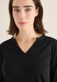 Schwarzes V-Ausschnitt-Oberteil aus einem weichen Stoff mit einem dezenten strukturierten Ausschnitt und Dreiviertelärmeln, entworfen für Komfort und Vielseitigkeit.