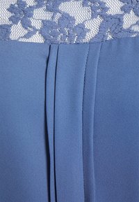 Vestido azul com um sobreponto de renda floral na parte superior e tecido suavemente pregueado na parte inferior. Textura lisa em todo o vestido.