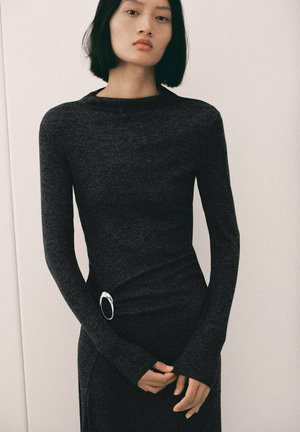 Vestido negro de manga larga hecho de tela texturizada, con una silueta ajustada y un acento plateado en la cintura. Diseño suave y minimalista.